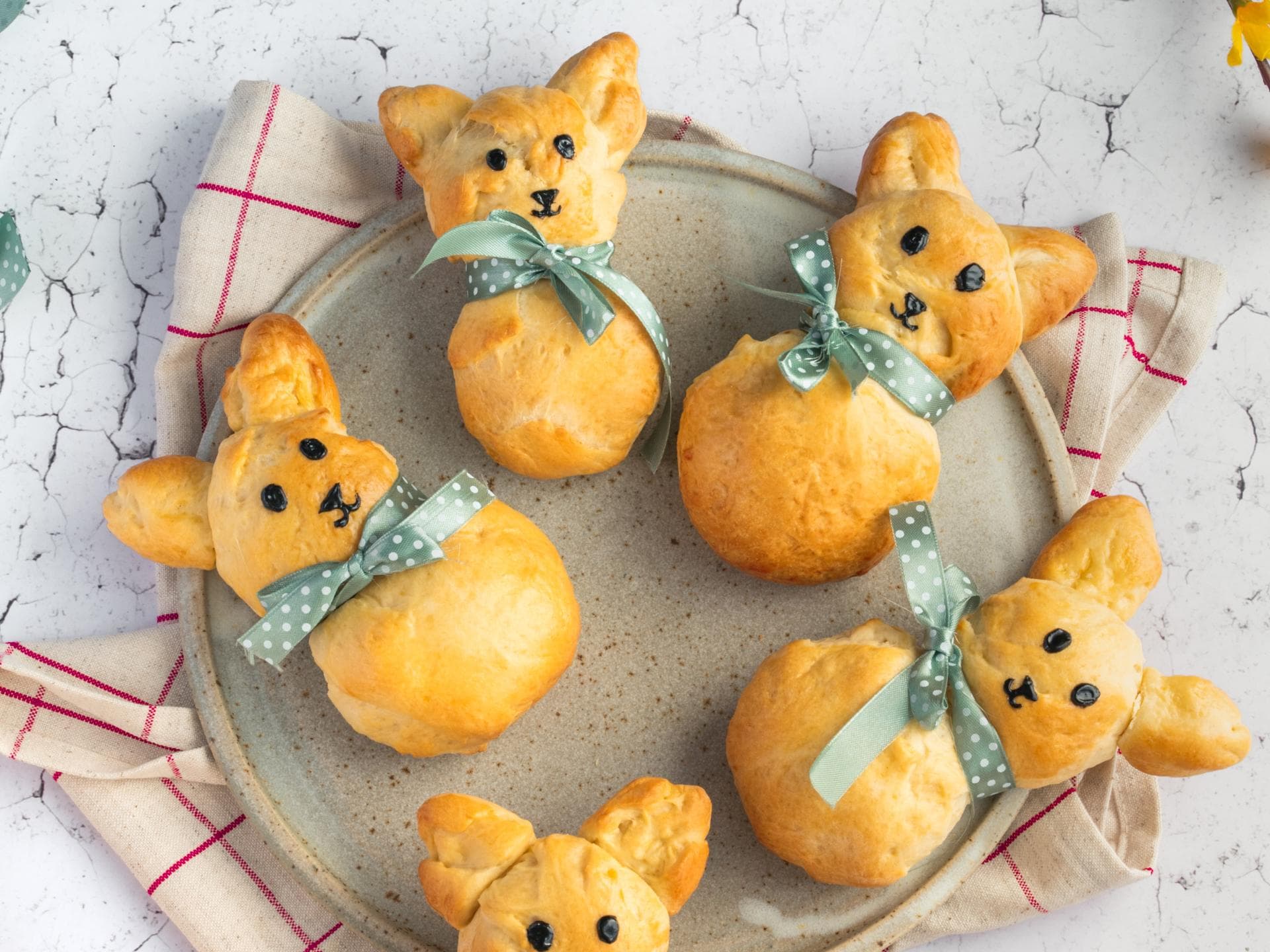 Fünf frisch gebackene Brioche-Häschen mit Schleife liegen auf einem Teller