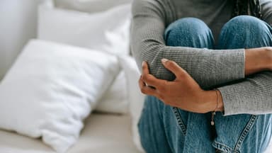 Brauche ich eine Therapie? Das sind die Anzeichen. Frau sitzt auf Bett mit angezogenen Knien.