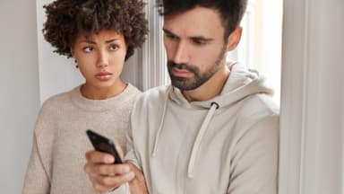 Betrogen zu werden ist ein großer Vertrauensbruch. Frau schaut Partner aufs Handy