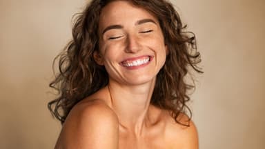 Gesunde Kopfhaut = Schöne, gesunde Haare Eine Frau mit gesundem, gelocktem Haar lacht zufrieden in die Kamera