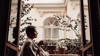 Mit den richtigen Kniffen wirkt selbst der kleinste Balkon größer Frau sitzt auf einem kleinen Balkon